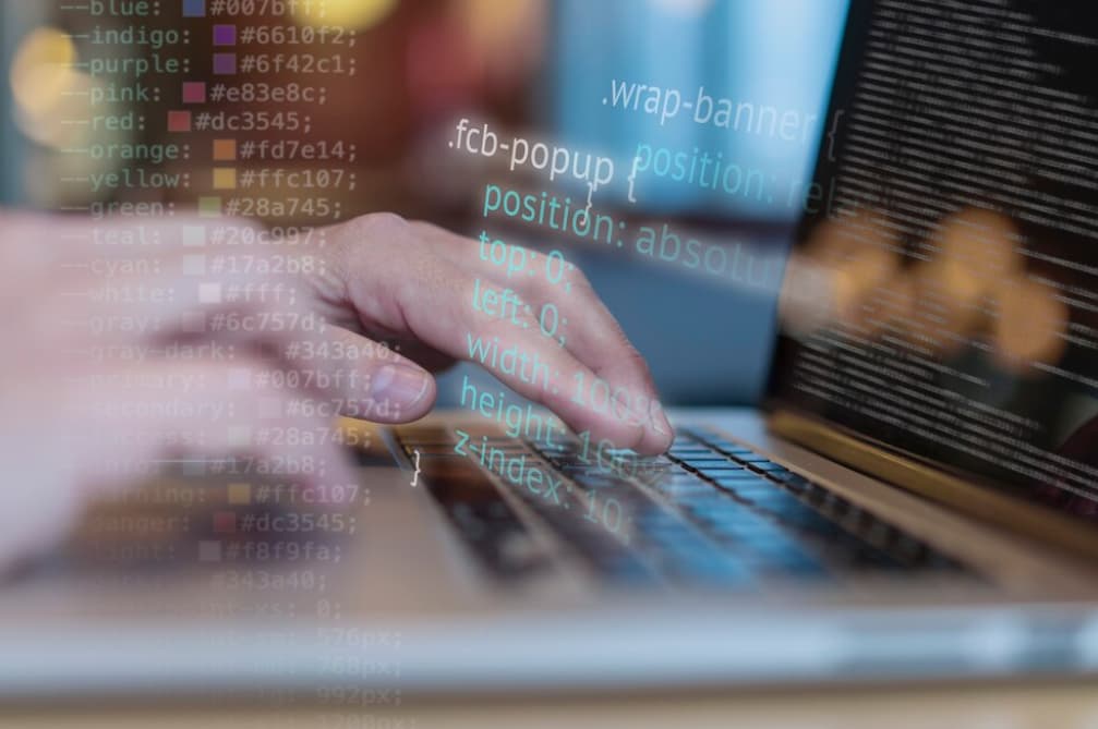 Close-up of a coder's hands typing with code overlay on the screen