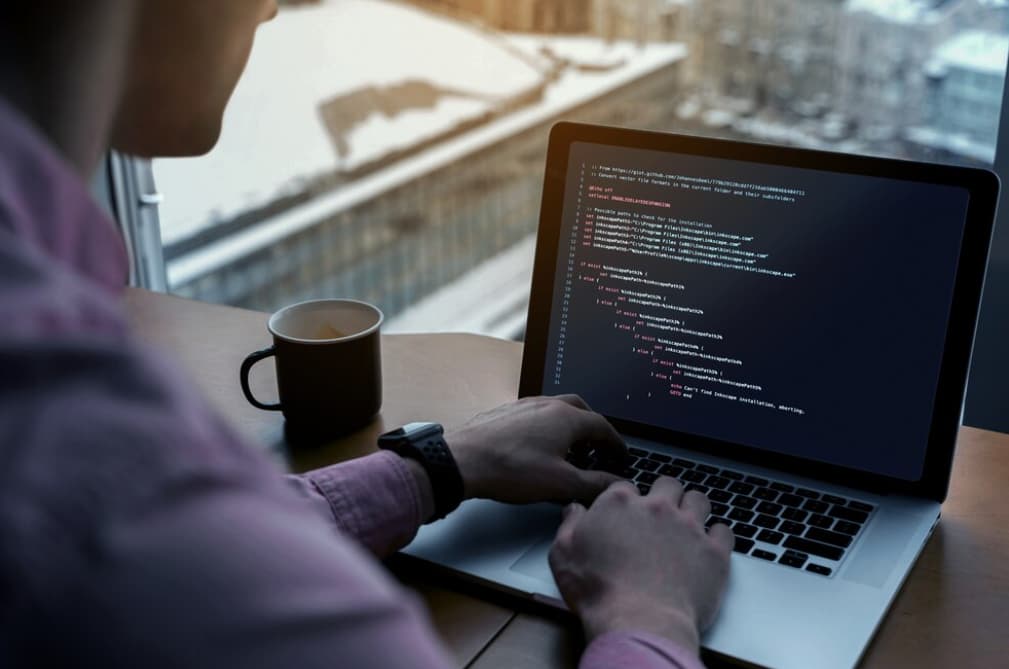 A person coding on a laptop with a cup of coffee beside them