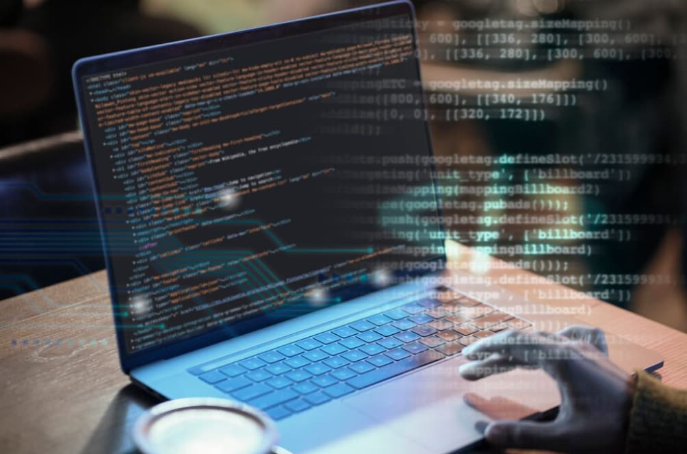 A person's hands typing on a laptop displaying coding software, overlaid with digital graphics