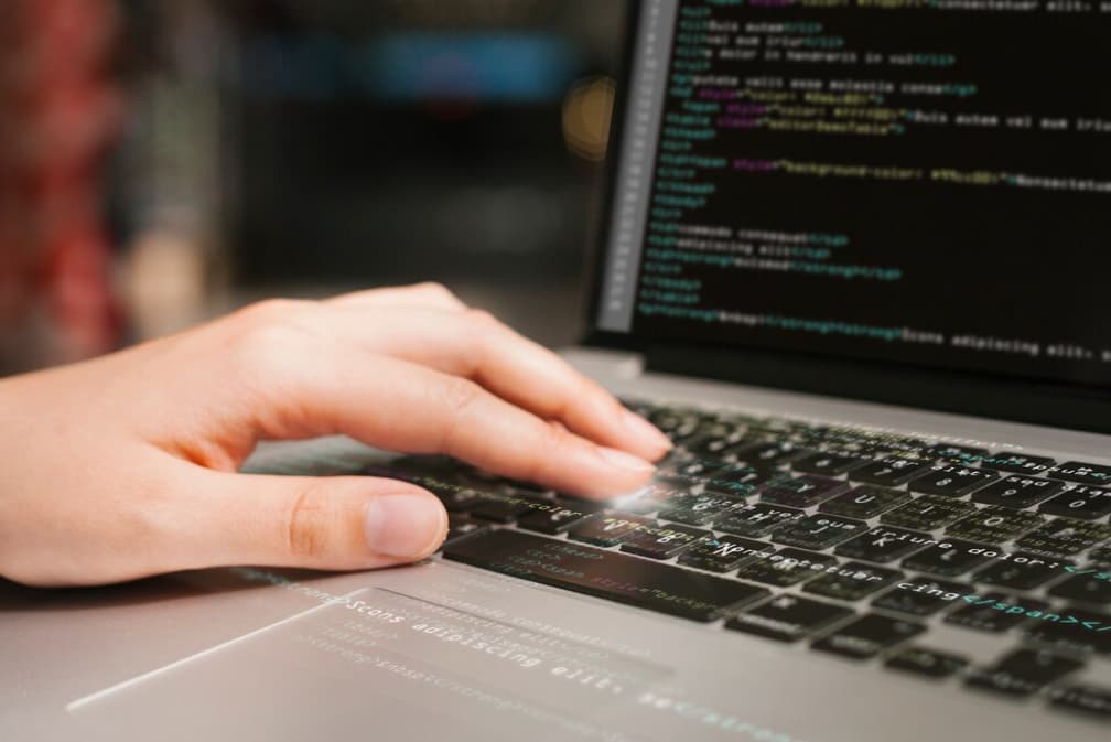 Close-up of hands typing on a laptop with code on the screen